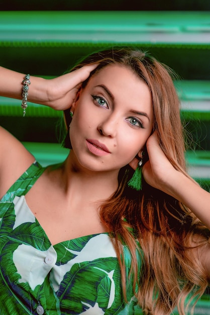 Retrato de mujer de cabello castaño con estilo en vestido verde aretes verdes con maquillaje sobre fondo verde