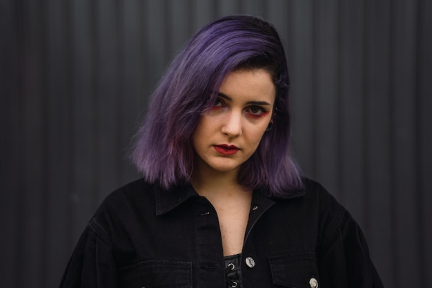 Retrato de una mujer con cabello morado y lápiz labial rojo sobre un fondo de pared negra