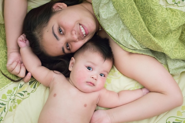 Foto retrato de una mujer sin camisa con su hijo tendido en la cama en casa