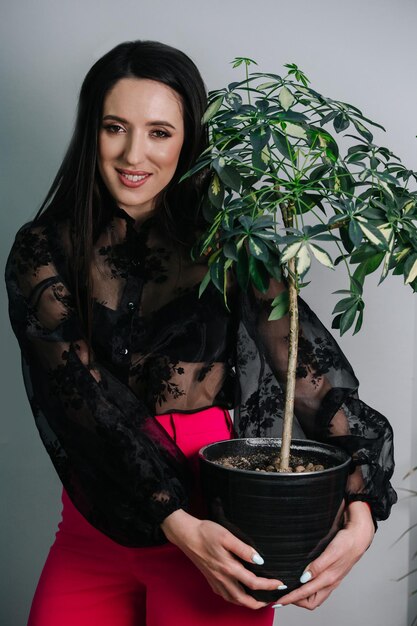 Retrato de una mujer con una camisa transparente y pantalones rojos sosteniendo una planta en maceta