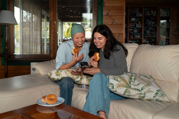 Foto retrato de una mujer con cáncer comiendo rosquillas con su amiga en casa