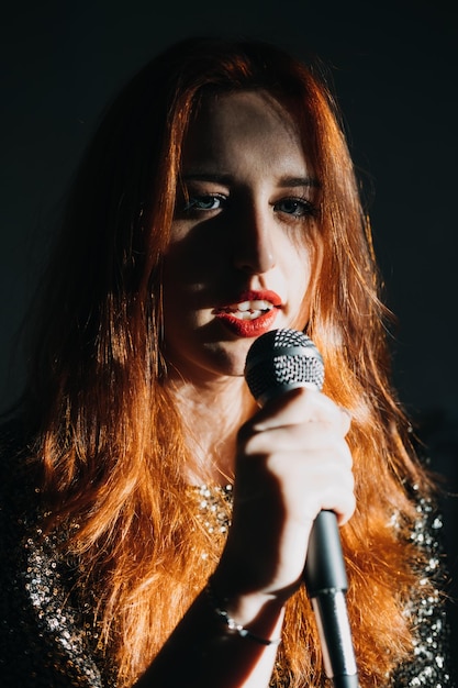 Retrato de mujer cantante pelirroja en vestido de noche brillante con cantante de micrófono en