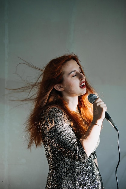 Retrato de mujer cantante pelirroja en vestido de noche brillante con micrófono