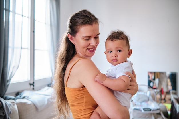 Retrato de una mujer cargando y sosteniendo a su bebé en brazos mientras lo mira y sonríe. Concepto de familia.