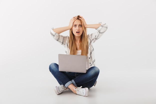 Retrato de mujer casual joven conmocionada con ordenador portátil