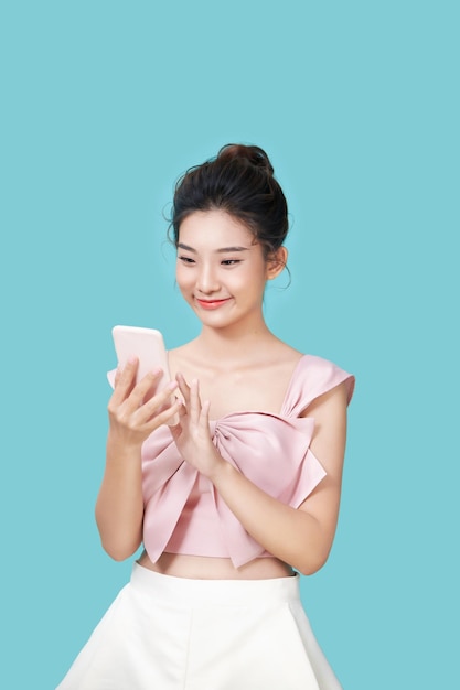 Retrato de una mujer casual sonriente sosteniendo un teléfono inteligente sobre fondo azul.