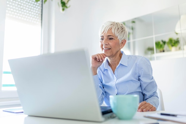 Retrato de mujer casual usando su computadora portátil mientras está sentado en la oficina en casa y trabajando. Una atractiva empresaria de mediana edad sentada frente a la computadora portátil y administrando su pequeña empresa desde casa.