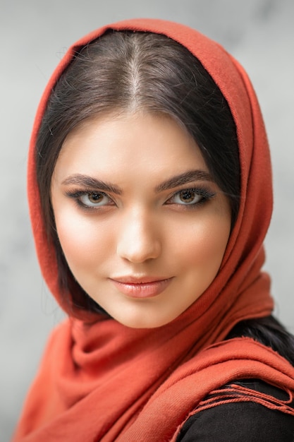 Foto retrato de una mujer caucásica bastante joven con maquillaje en un pañuelo rojo sobre fondo gris.