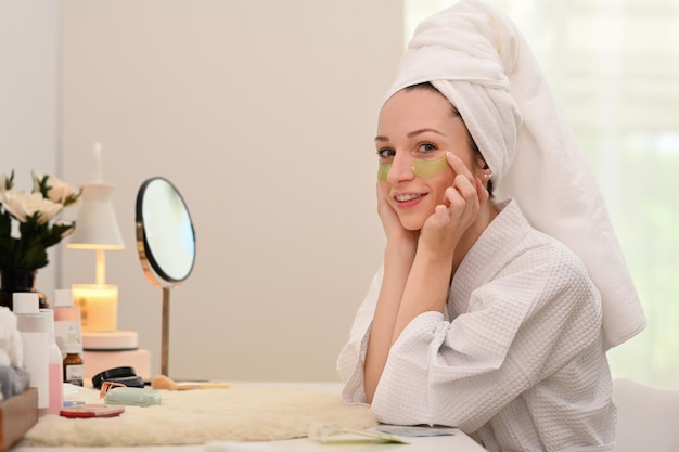 Retrato de mujer caucásica en bata de baño aplicando antifatiga debajo de los ojos Tratamiento de belleza y concepto de autocuidado