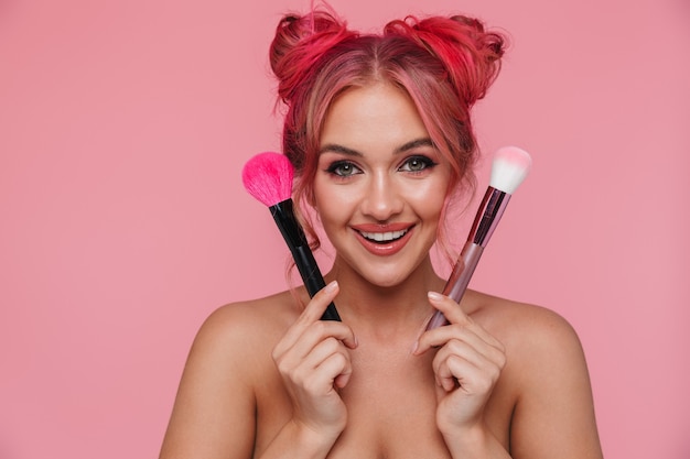 Retrato de mujer caucásica sin camisa con peinado colorido con pinceles de maquillaje