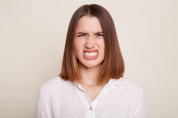 Retrato de una mujer caucásica enfadada caucásica con camiseta posando aislada sobre fondo blanco emociones agresivas mirando la cámara con los dientes apretados