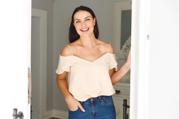 Foto retrato de una mujer caucásica feliz parada en la puerta, saludando a un visitante y sonriendo