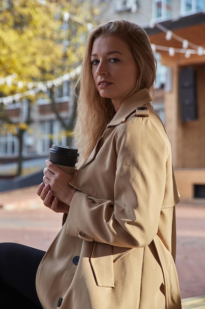 Retrato de mujer caucásica en gabardina beige al aire libre con una taza de café