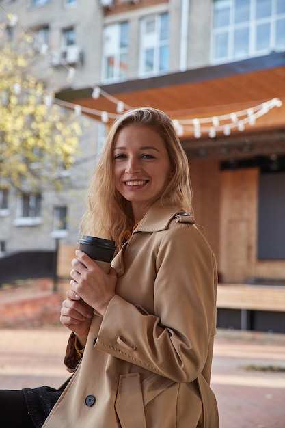 Retrato de mujer caucásica en gabardina beige al aire libre con una taza de café