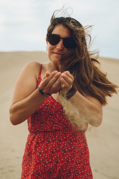 Retrato de una mujer caucásica con gafas de sol con arena cayendo de sus manos