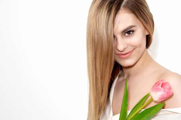 Retrato de una mujer caucásica joven feliz con un tulipán rosa sobre un fondo blanco con espacio de copia