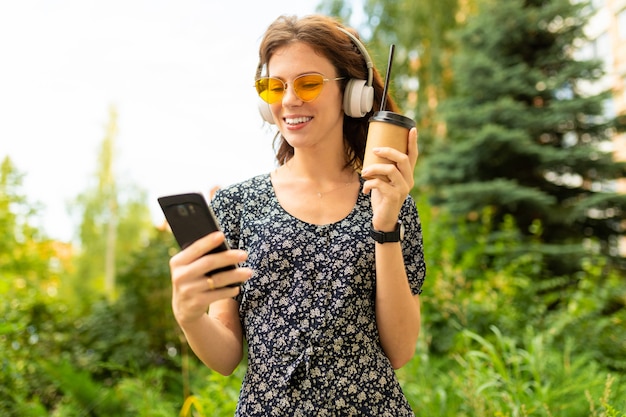 Un retrato de una mujer caucásica joven con una sonrisa perfecta, labios carnosos, anteojos, auriculares, paseos por la naturaleza y bebidas café