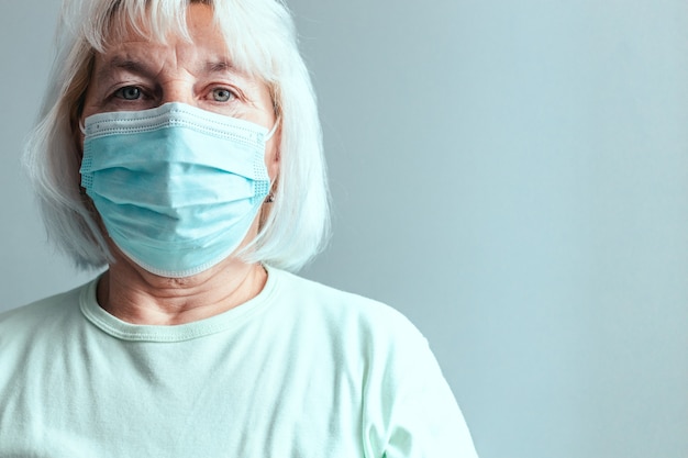 Retrato de mujer caucásica en una máscara médica aislada sobre un fondo de pared gris.