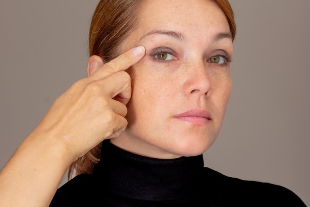 Foto retrato de una mujer caucásica de mediana edad recortada con pecas en el párpado con el dedo en