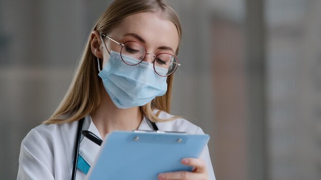 Retrato mujer caucásica médico enfermera en máscara médica escribir información diario de registro