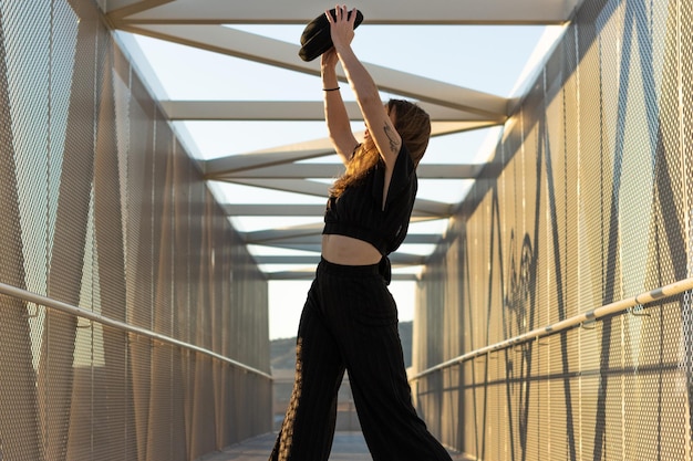 Retrato de una mujer caucásica con sombrero bailando danza urbana contemporánea en la calle al atardecer en un estilo de baile waacking de puente