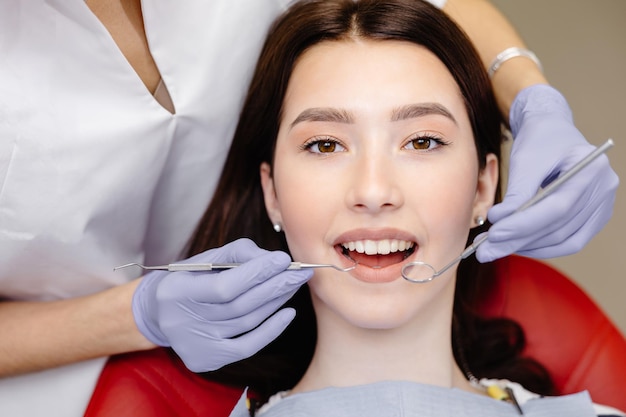 Retrato de mujer caucásica sonriente y manos de dentista recortadas en guantes azules con herramientas en las manos