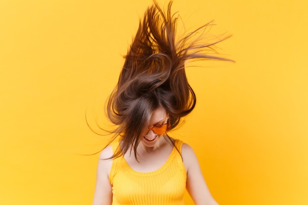 Retrato de mujer cómica divertida de risa alegre emocionada en gafas naranjas con espacio de copia de cabello revoloteando aislado sobre fondo amarillo. Personas sinceras emociones, concepto de estilo de vida. Área de publicidad.