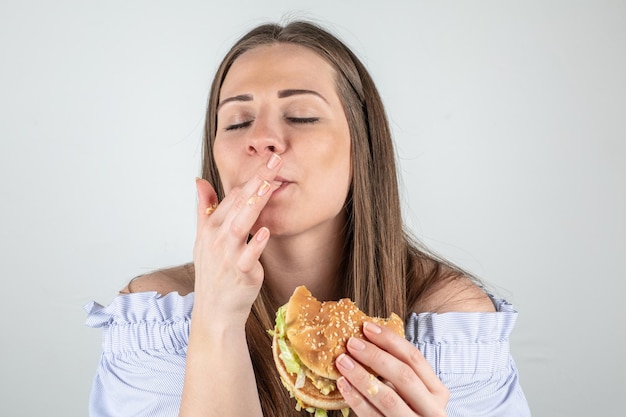 Foto retrato de una mujer comiendo una hamburguesa contra un fondo blanco