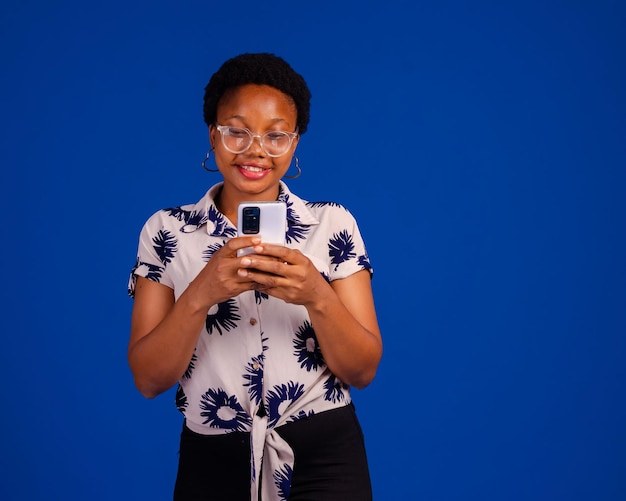 Retrato de mujer complacida sonriendo y usando teléfono móvil aislado sobre fondo azul.