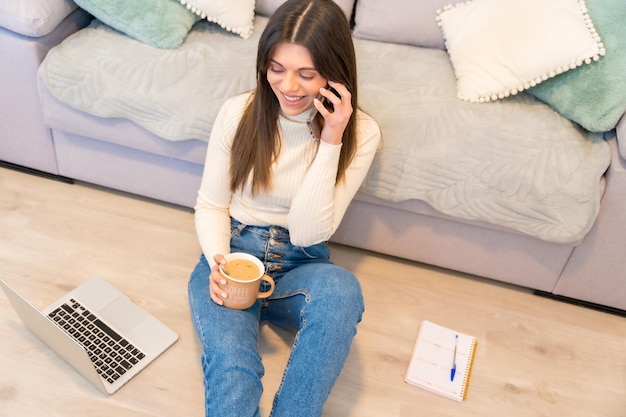 Retrato de una mujer con una computadora sentada en un sofá con un café caliente hablando por teléfono blog de redes sociales del milenio