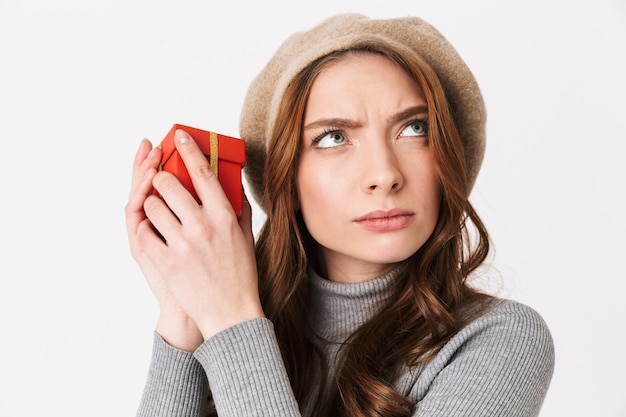 Retrato de mujer concentrada de 30 años con sombrero con caja de regalo roja aislado en blanco