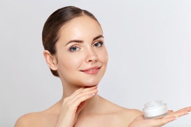 Retrato de mujer, concepto de cuidado de la piel, piel hermosa y manos sosteniendo y aplicando crema hidratante. Tratamiento facial. Cosmetología, belleza y spa.