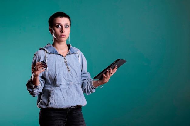 Retrato de una mujer confundida y preocupada escribiendo los detalles de la tarjeta de crédito en una tableta, teniendo problemas después de ver el precio del pedido. Persona interesada haciendo costosas compras en línea en el estudio