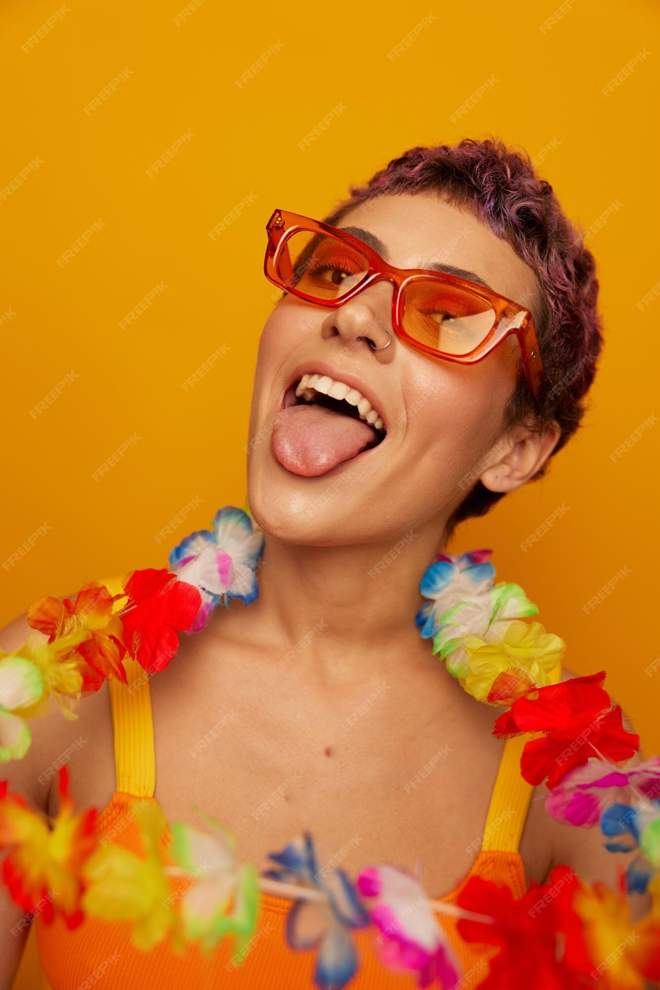 Retrato de una mujer con una floral hawaiana alrededor de su se divierte bailando y sonriendo con ropa brillante en un fondo naranja con gafas de sol estilo hawaiano