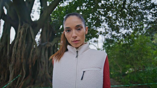 Retrato de una mujer deportiva mirando a la cámara preparándose para una rutina de entrenamiento en un parque verde