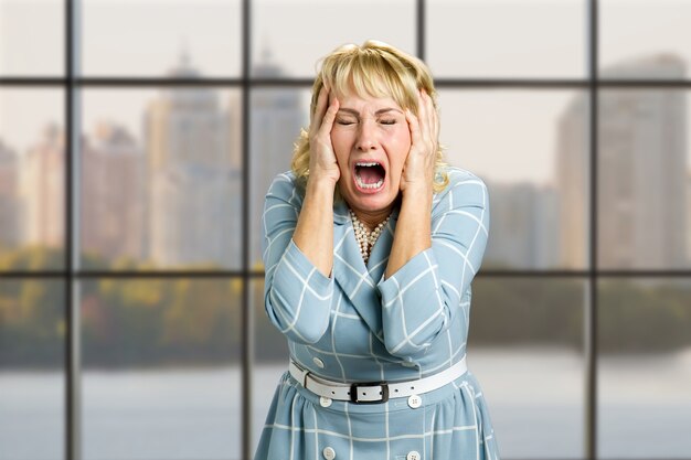 Retrato de mujer desesperada gritando. Primer plano de mujer estresada y frustrada gritando con expresión desesperada y horrorizada, ventana de la oficina.