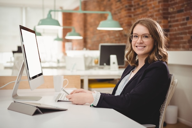 Retrato de mujer ejecutiva sonriente mediante teléfono móvil mientras trabaja en la computadora