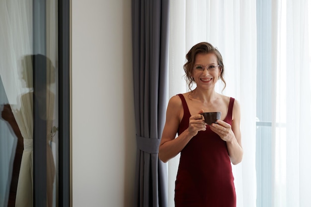 Retrato de mujer elegante madura sosteniendo una taza de café y sonriendo a la cámara