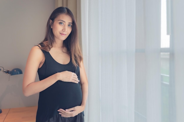 Retrato de mujer embarazada asiática en el dormitorio