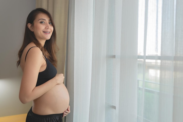Retrato de mujer embarazada asiática en el dormitorio