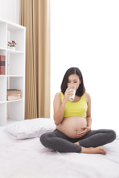 Retrato de mujer embarazada bebiendo un vaso de leche fresca en casa