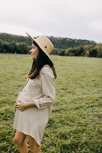 Retrato de una mujer embarazada con cabello moreno al aire libre en la naturaleza con un sombrero de paja