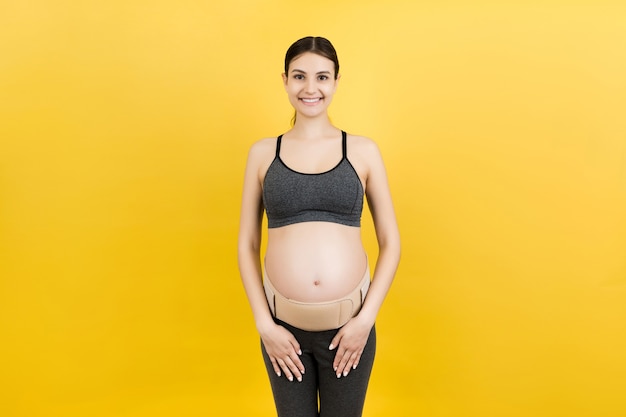 Retrato de mujer embarazada con cinturón de embarazo en fondo amarillo con espacio de copia. Concepto de cinturón de soporte abdominal ortopédico.