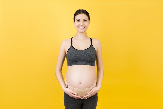 Retrato de mujer embarazada con cinturón de maternidad para reducir el dolor en la espalda en fondo amarillo con espacio de copia. Concepto de cinturón ortopédico de soporte abdominal