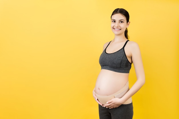 Retrato de mujer embarazada con corsé de embarazo contra el dolor de espalda en fondo amarillo con espacio de copia. Concepto de cinturón de soporte abdominal ortopédico.