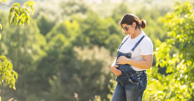 Retrato de una mujer embarazada feliz y orgullosa mirando su vientre en un parque al amanecer con una cálida luz de fondo en el fondo