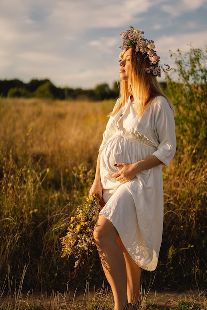 Retrato de una mujer embarazada una hermosa joven embarazada con un vestido blanco camina en el campo