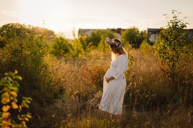 Retrato de una mujer embarazada una hermosa joven embarazada con un vestido blanco camina en el campo