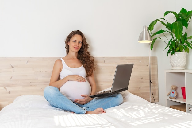 Foto retrato de una mujer embarazada de pelo largo sentada en el sofá interior sala doméstica con portátil