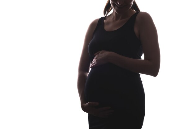 Retrato de mujer embarazada sonriente en vestido negro sobre fondo blanco, concepto de embarazo feliz